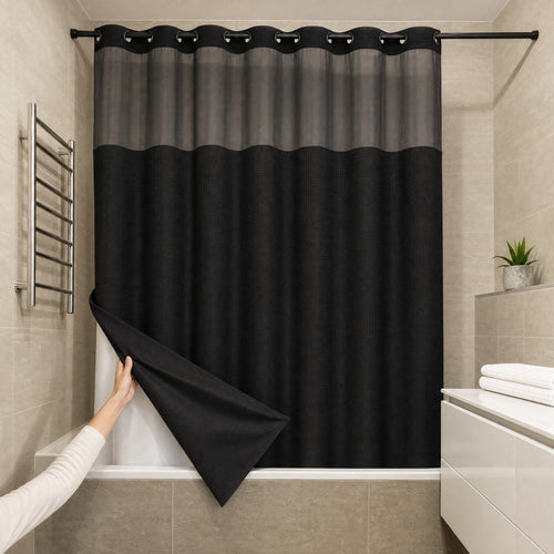 Une main relève le coin du rideau de douche Aqualis™ noir et découvre sa doublure blanche, dans une salle de bain carrelée