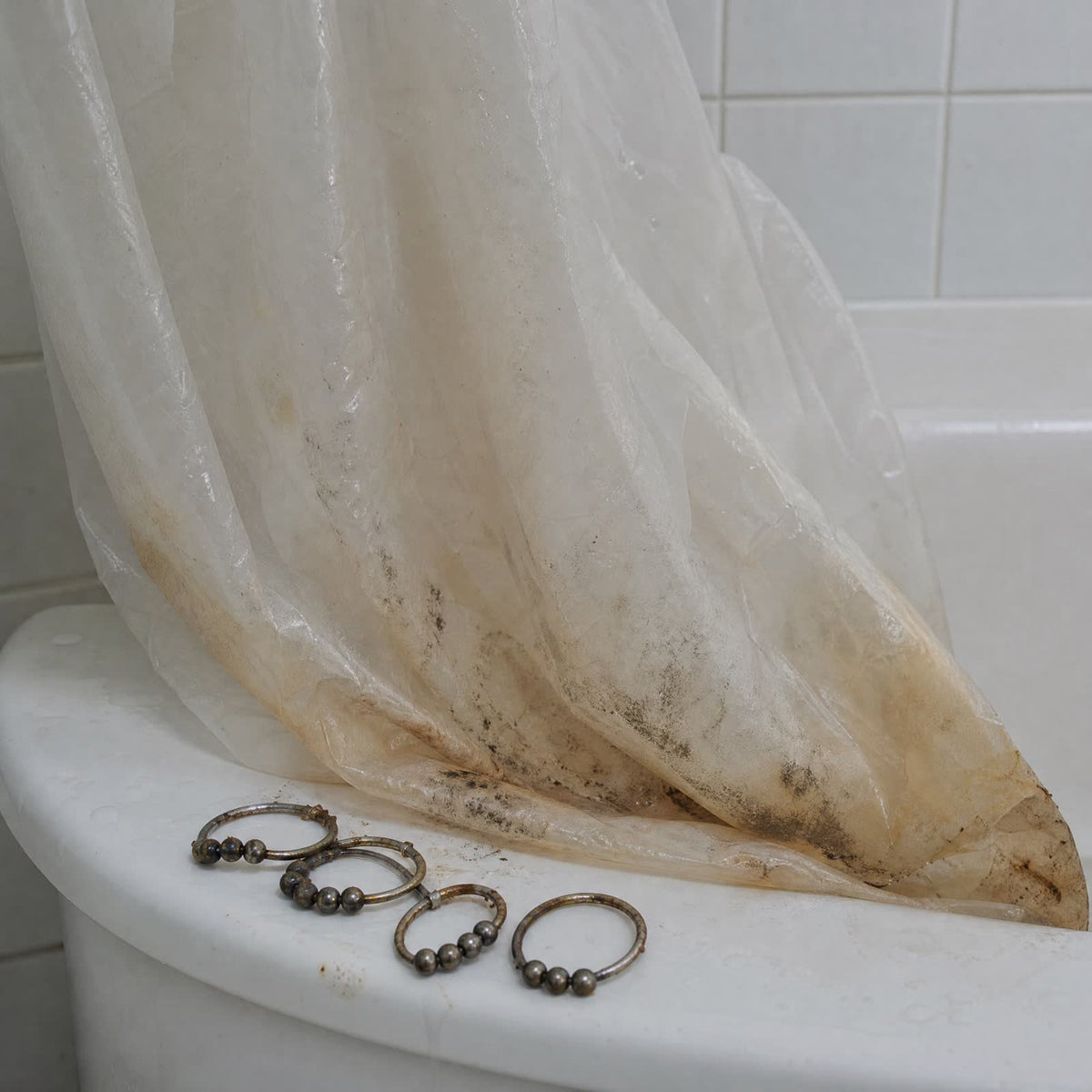 Vieille doublure de douche en plastique tachée de moisissure et crochets rouillés au bord de la baignoire