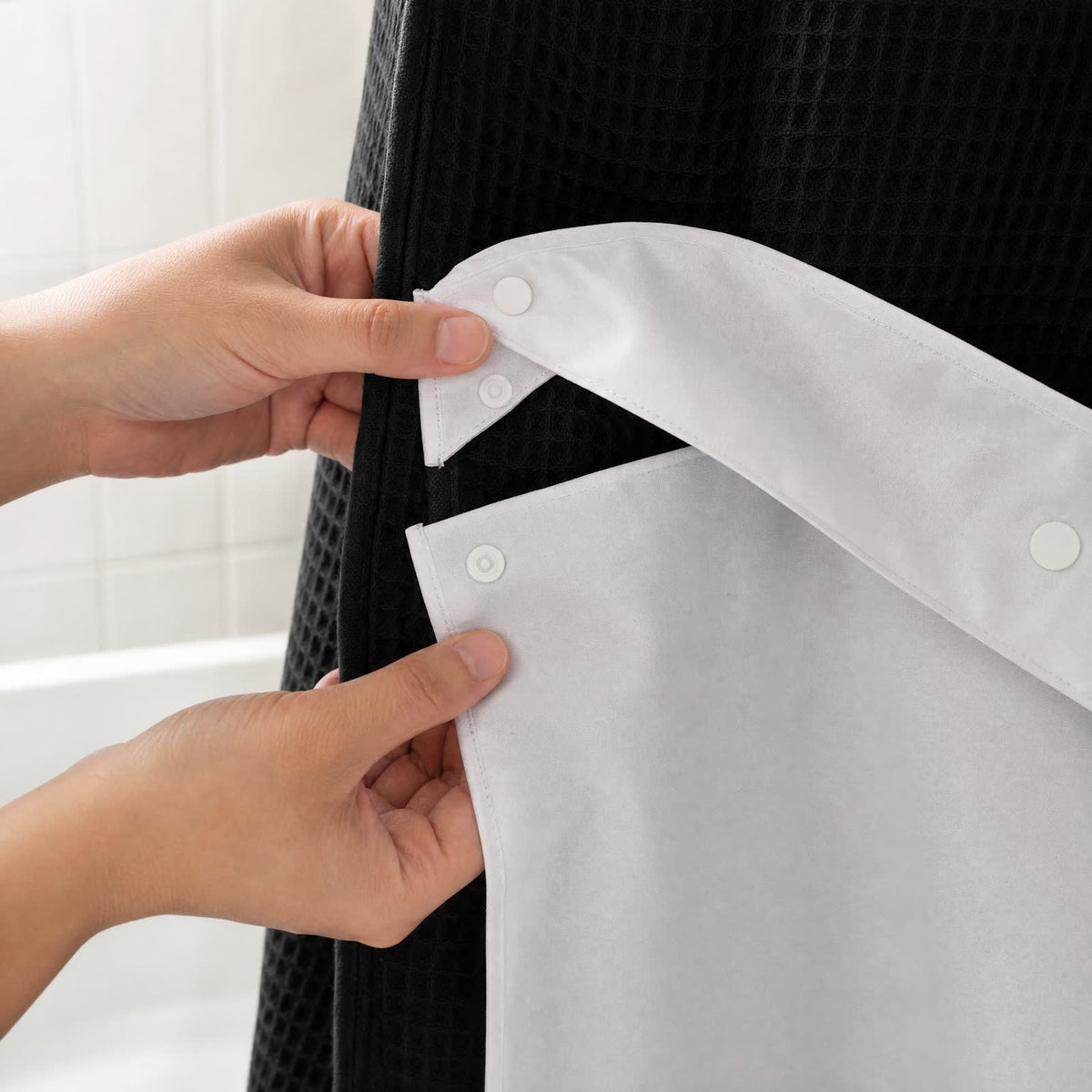 Deux mains détachent par ses pressions la doublure blanche du rideau Aqualis™ noir