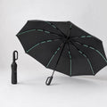 Parapluie Tokyo™ noir, ouvert en trois quarts et plié debout, sur fond studio clair.